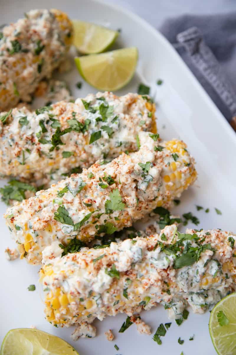 A plate of Mexican street corn topped with cilantro and garnished with lime slices on the side.