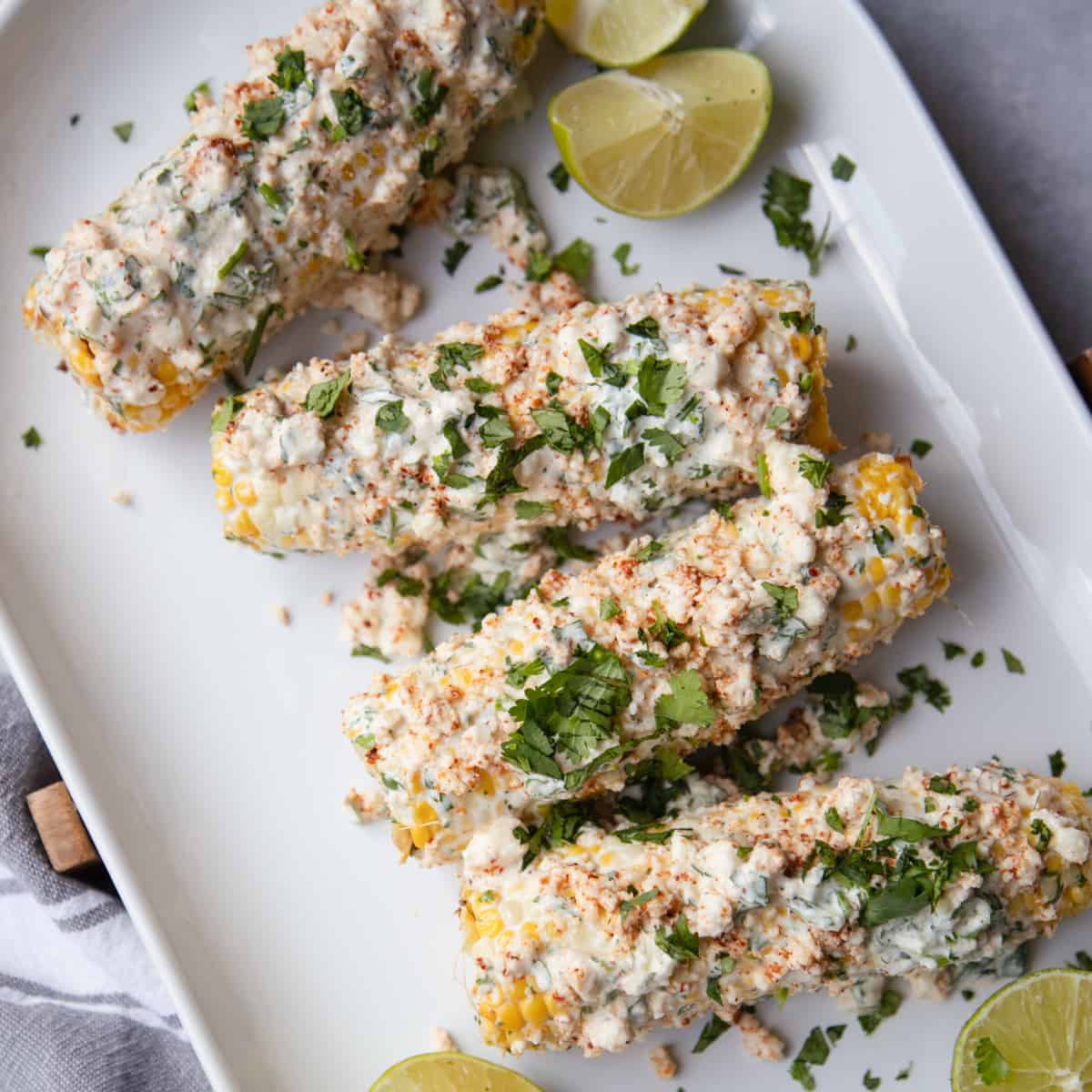 A plate of Mexican street corn topped with cilantro and garnished with lime slices on the side.