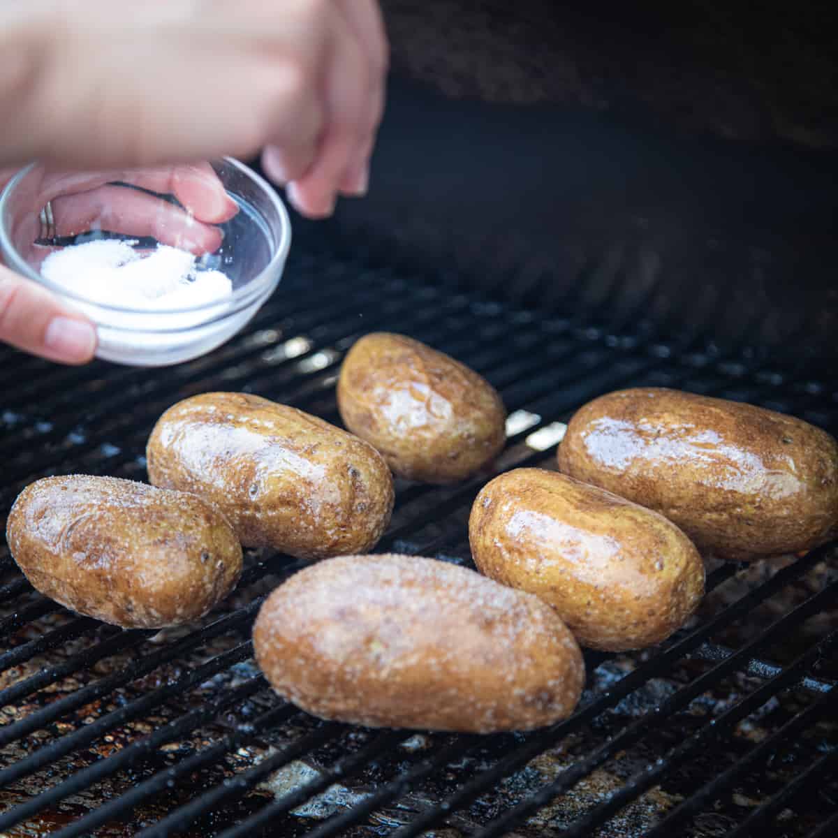 Salt being sprinkled on potatoes on a Traeger grill. 