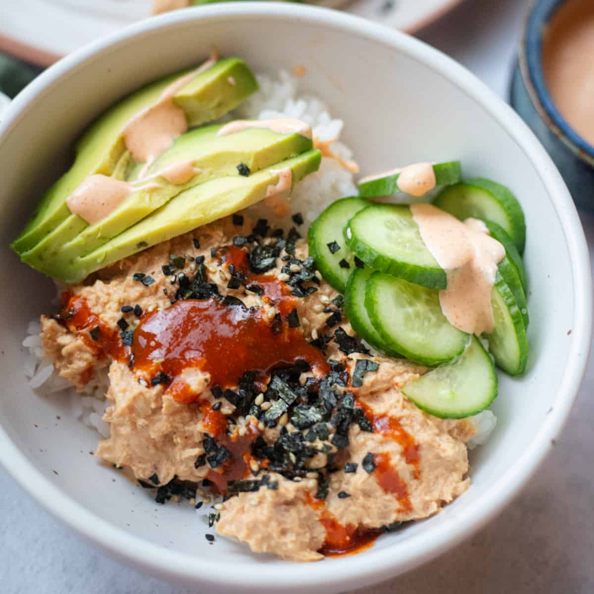 Spicy canned tuna on top of rice with avocado and cucumber on the side. 