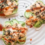 Spicy canned tuna on a rice stacker with cucumbers and avocado and topped with spicy mayo, sriracha, sesame seeds, and nori.