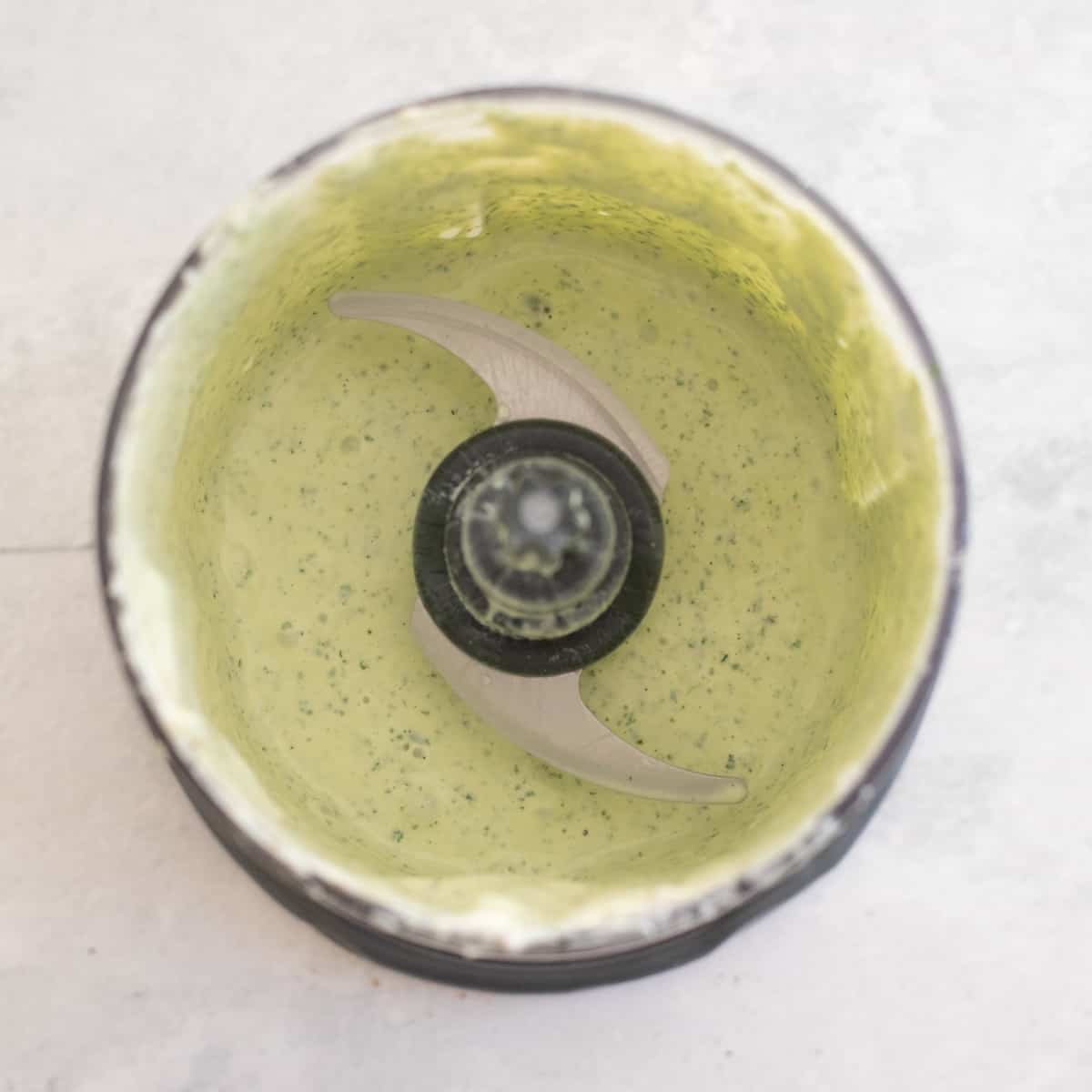 Cilantro ranch blended in a food processor. It's light green in color with dark green specks. 