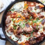 A cast-iron pan full of meatballs and peppers, topped with melted mozzarella cheese and fresh basil.