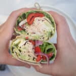 Hands holding two halves of a pesto turkey wrap stuffed with turkey, lettuce, roasted red peppers, onions, and cheese.