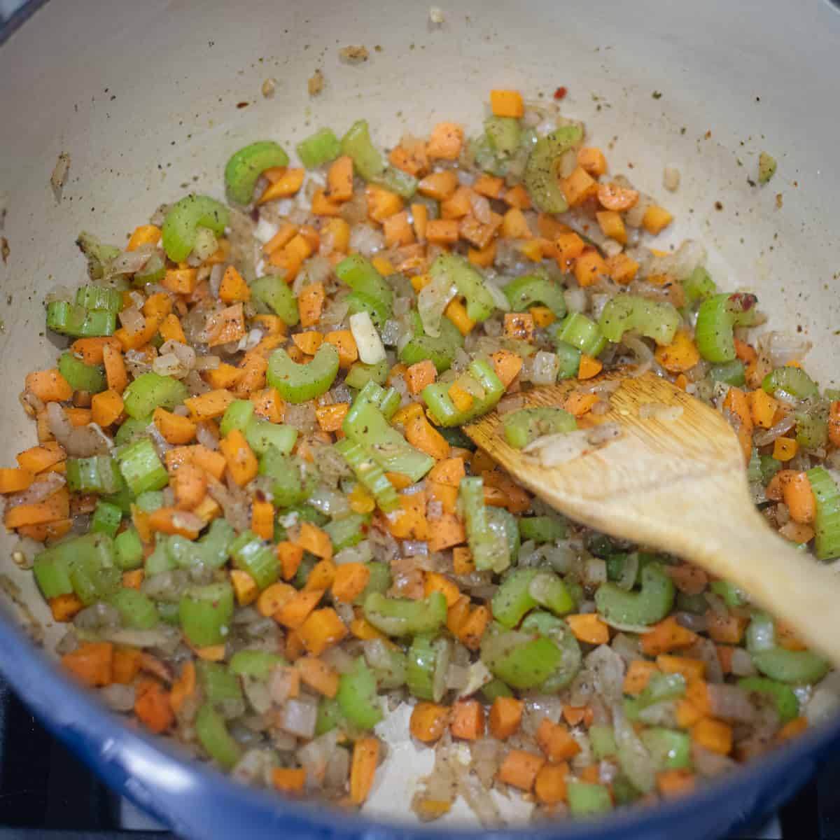 Onions, celery, carrots, and garlic cooking in a dutch oven. 