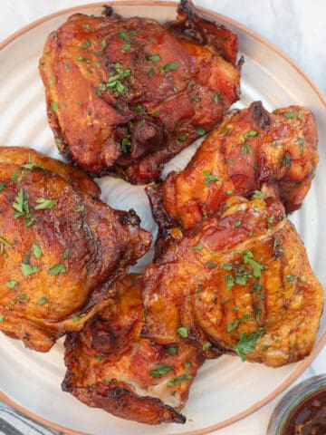 A plate of orange-colored Traeger smoked chicken thighs. They're topped with chopped green parsley.
