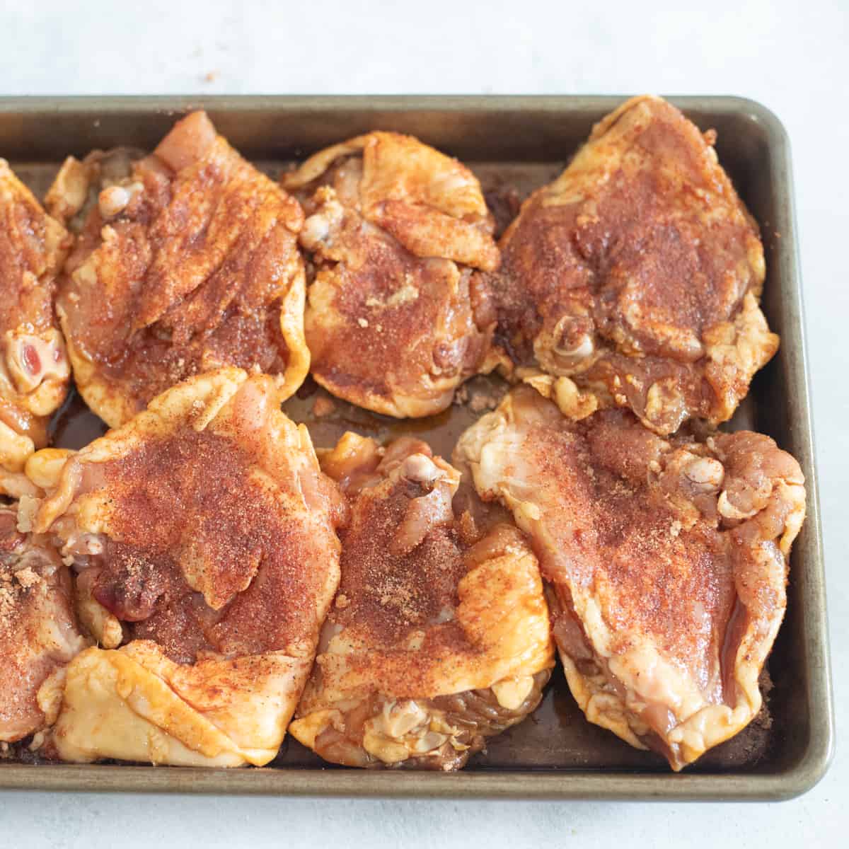 Raw chicken thighs on a sheet pan with seasoning on top of them.