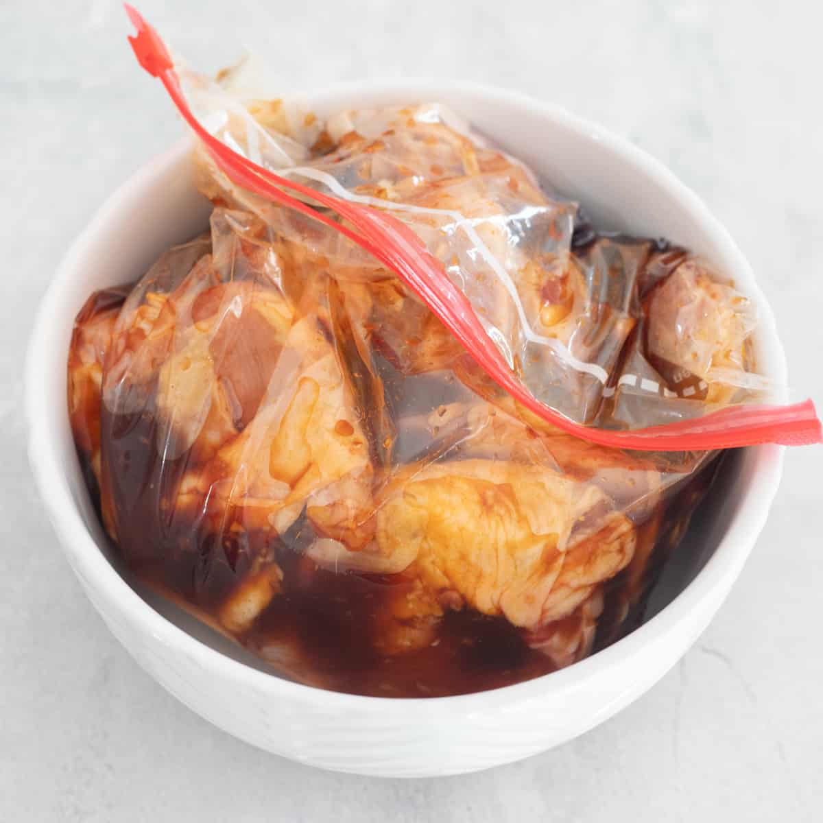 Chicken thighs in a gallon baggie in a dark brown-ish orange marinade. 