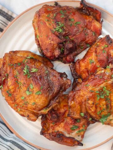 A plate of orange-colored Traeger smoked chicken thighs. They're topped with chopped green parsley.