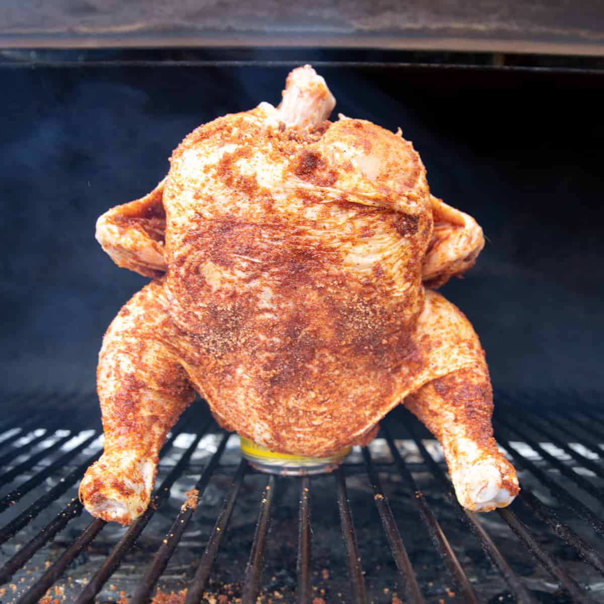 An uncooked chicken sitting on top of a beer can on a grill. 