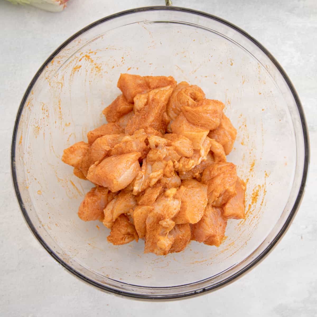 Chunks of raw chicken breast in a mixing bowl coated with taco seasoning. 