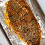 A whole cooked salmon on top of an aluminum foil-coated pan. The salmon is topped with spices and fresh dill.
