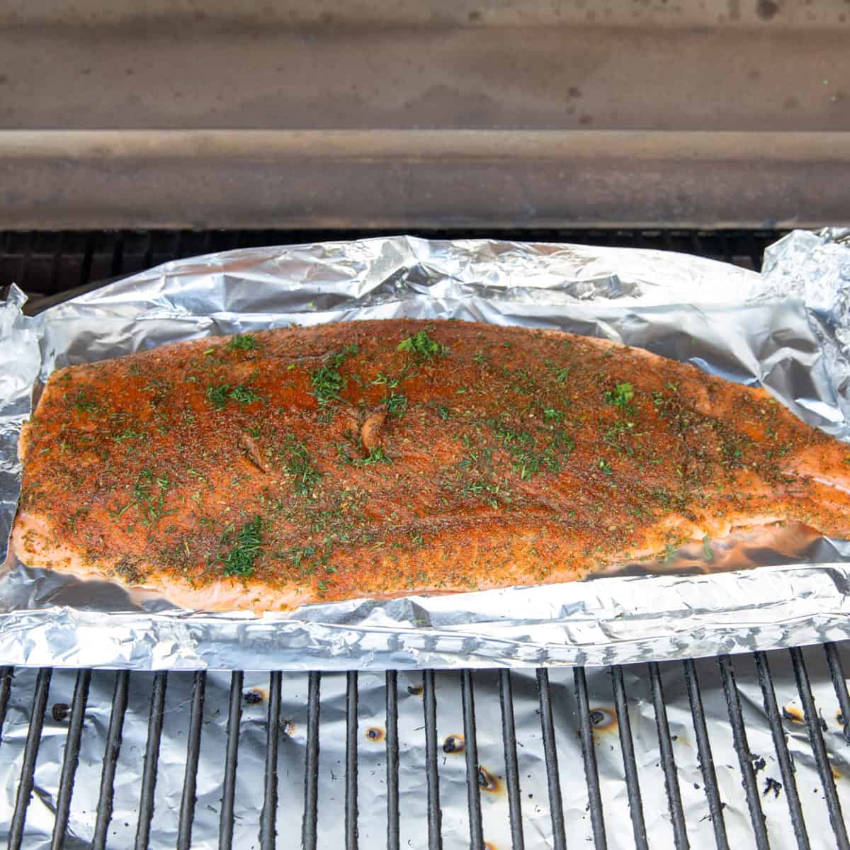 A whole salmon fillet cooking on a Traeger. It's topped with a variety of spices and fresh dill. 