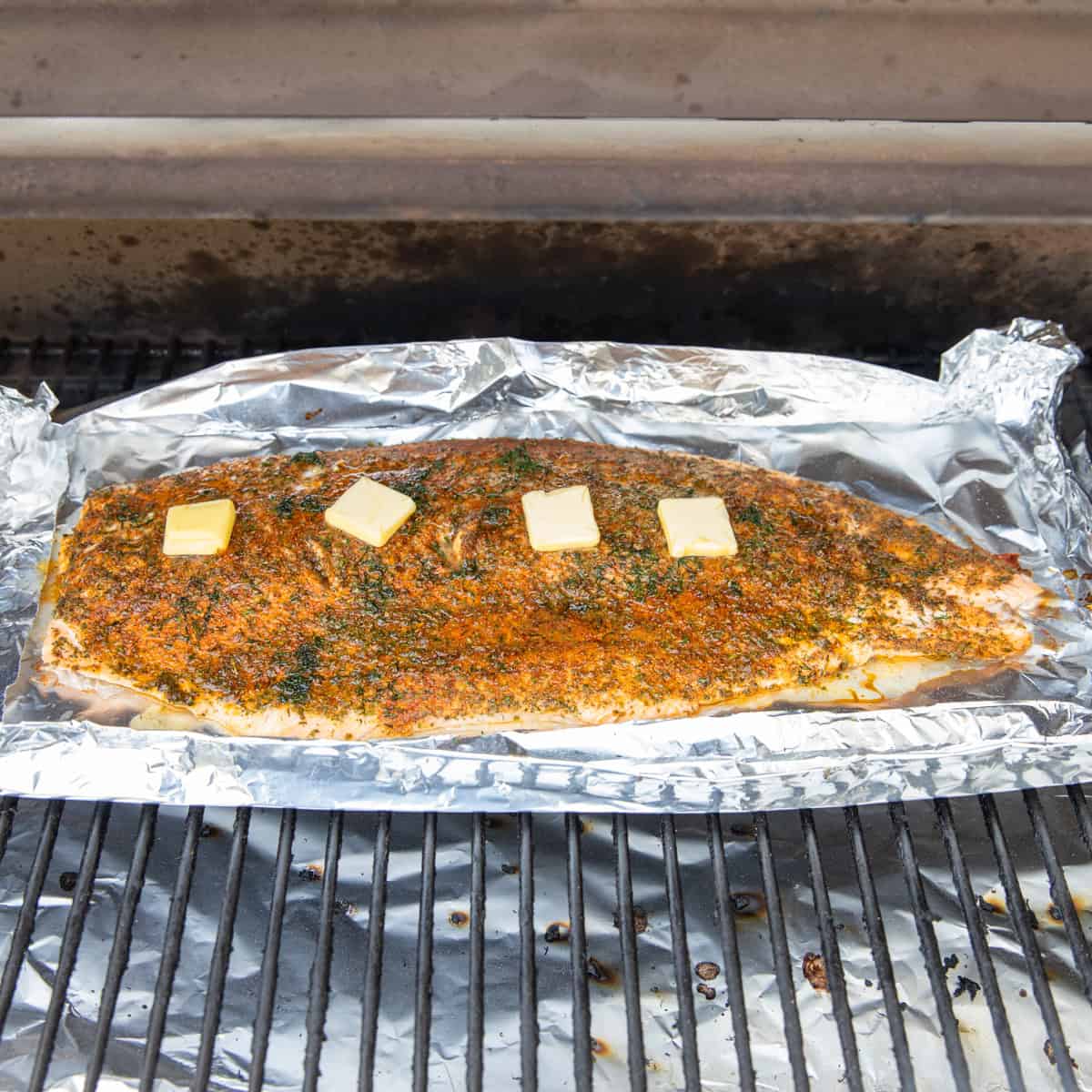 Salmon cooking on the Traeger topped with several pats of butter. 