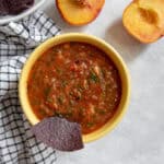 A bowl of red salsa with chunks of tomatoes, peach, mango, and cilantro.