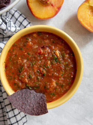 A bowl of red salsa with chunks of tomatoes, peach, mango, and cilantro.