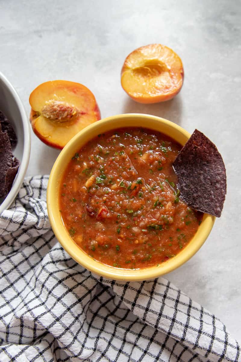 A bowl of red salsa with chunks of tomatoes, peach, mango, and cilantro.