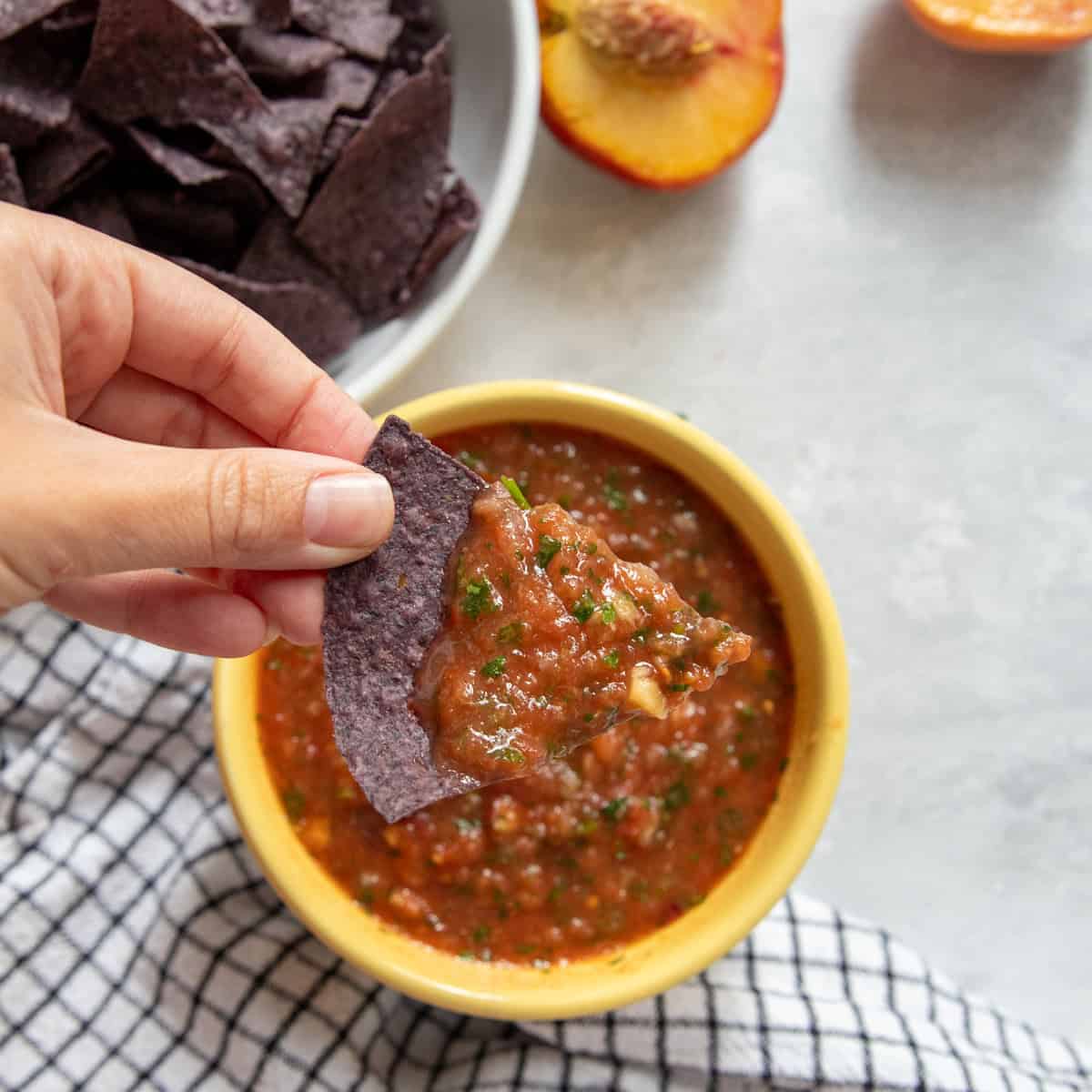 A hand with a chip scooping up red salsa. 