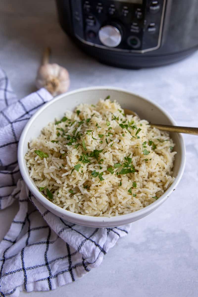 A bowl of basmati rice in a serving bowl topped with fresh parsley. There is an instant pot in the background. 