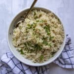 A bowl of basmati rice in a serving bowl topped with fresh parsley.