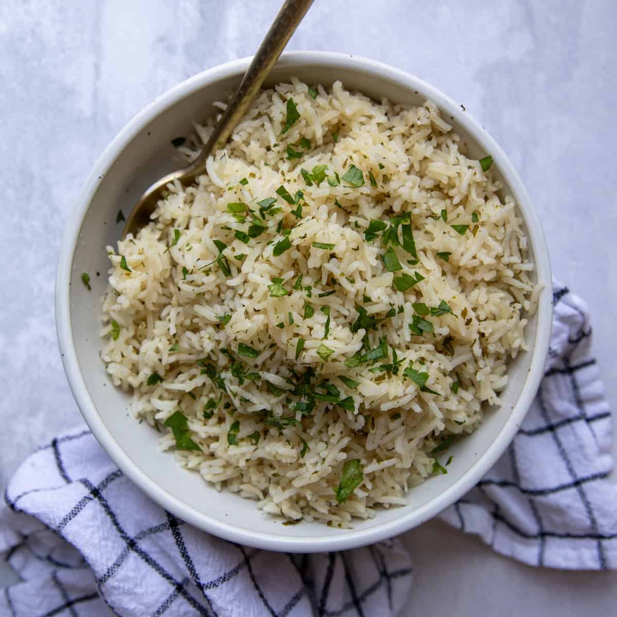 A bowl of basmati rice in a serving bowl topped with fresh parsley.