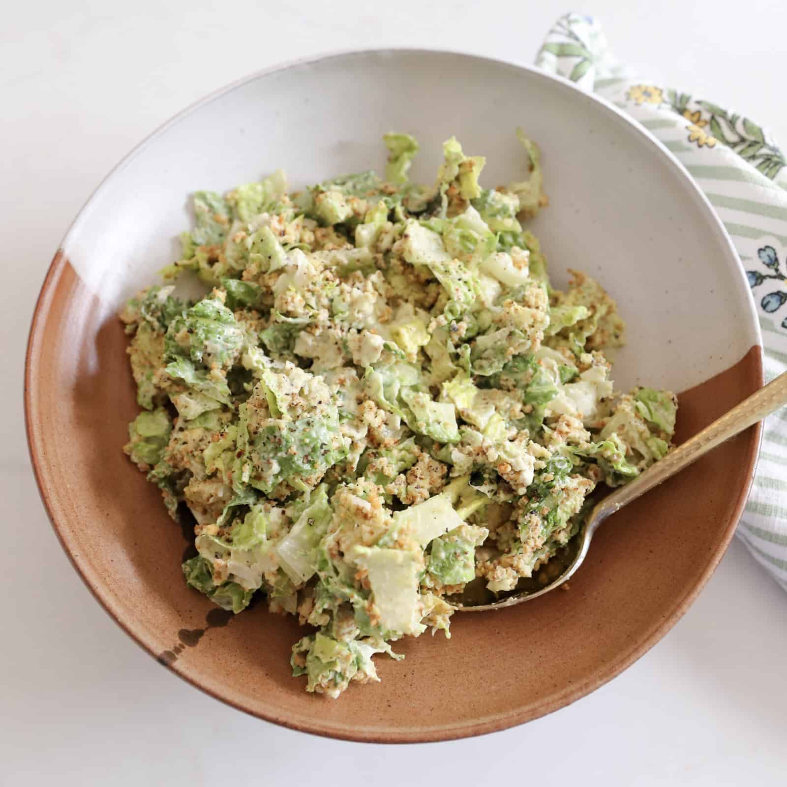 All the ingredients for avocado Caesar salad arranged on a countertop, including romaine, avocado, parmesan, anchovies, Greek yogurt, mayo, lime, garlic, Dijon, butter, and panko.