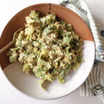 A serving bowl filled with avocado Caesar salad topped with toasted panko and parmesan, with a kitchen towel beside it.
