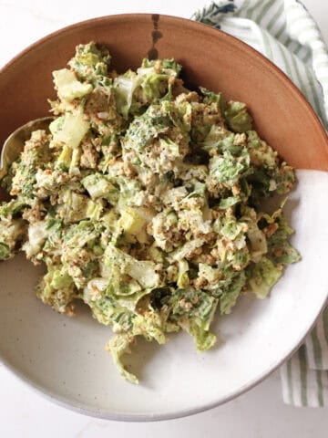 A serving bowl filled with avocado Caesar salad topped with toasted panko and parmesan, with a kitchen towel beside it.